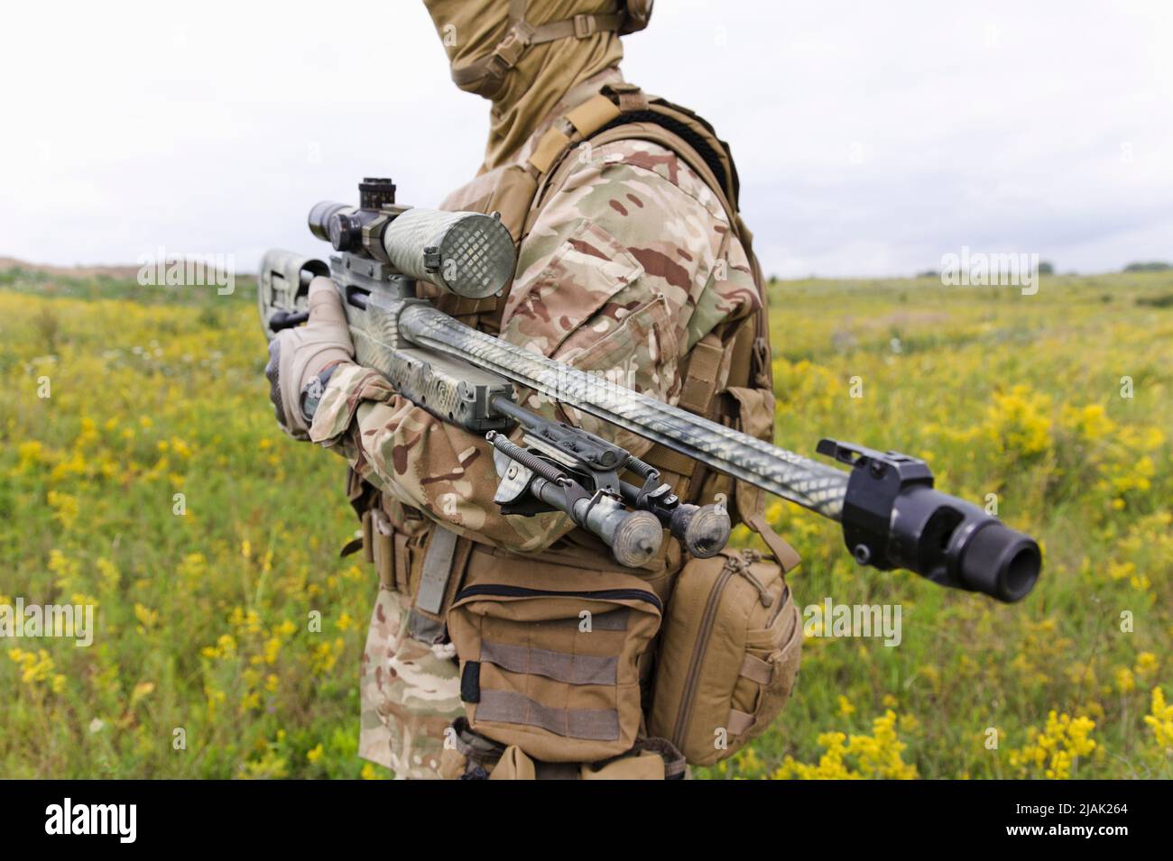 Soldat avec un fusil de sniper debout dans un champ vert en fleur. Banque D'Images