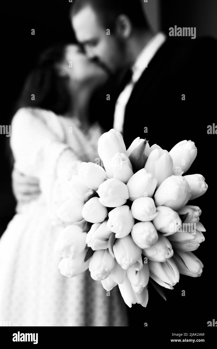 Embrasser un jeune couple avec un bouquet de fleurs de tulipes blanches en noir et blanc image, sélectif foyer. Photo verticale. Banque D'Images