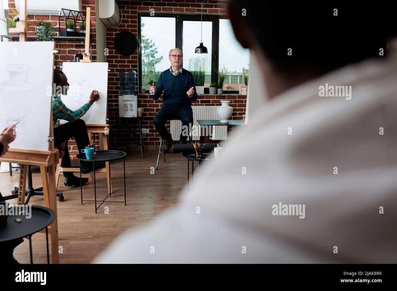 Diverses équipes esquissant un modèle de vase sur toile blanche pendant le cours d'art apprenant comment ro dessiner pour la croissance personnelle. Homme enseignant expliquant la technique de dessin aux élèves. Concept d'activité créative Banque D'Images