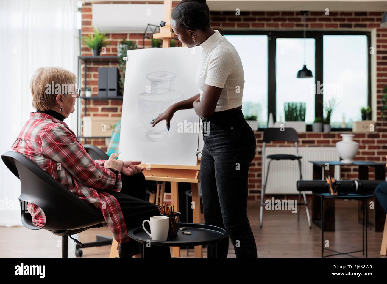 Professeur d'art afro-américain expliquant la technique de dessin à l'étudiant senior pendant le cours de créativité. Artiste femme esquissant un modèle de vase sur toile blanche à l'aide d'un crayon graphique. Résolutions du nouvel an Banque D'Images