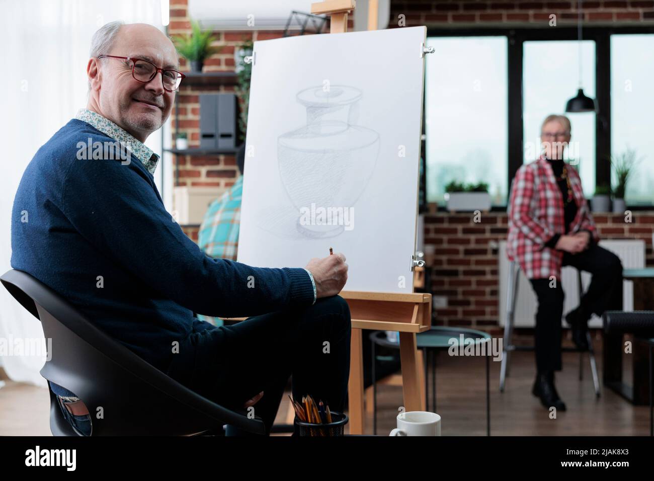 Portrait d'un artiste senior souriant debout devant sur toile blanche dessinant un vase artistique à l'aide d'une technique d'esquisse pendant la leçon d'art en studio de créativité. Peintre âgé havnig hobby créatif Banque D'Images