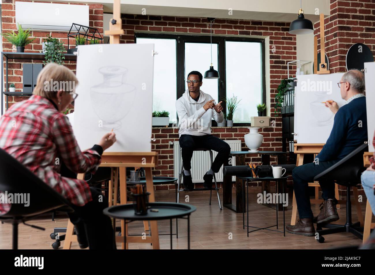 Homme enseignant expliquant la technique de l'illustration graphique aux élèves pendant les cours d'art en studio de créativité. Équipe multiethnique dessin vase croquis sur toile blanche apprentissage de nouvelles compétences d'esquisse Banque D'Images