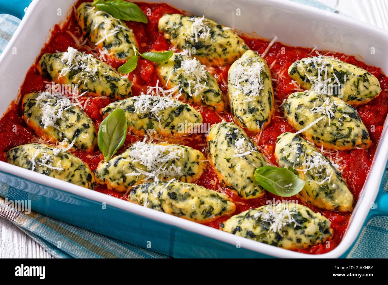Boulettes de ricotta aux épinards italiens sauce tomate aux herbes et parmesan râpé dans un plat de cuisson en céramique sur table blanche, gros plan Banque D'Images