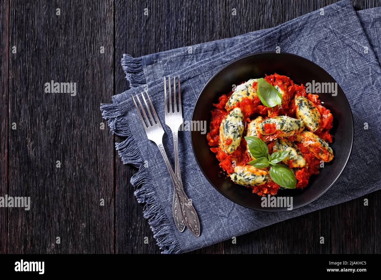 Boulettes de ricotta aux épinards italiens, sauce tomate aux herbes et parmesan râpé dans un bol noir sur une table en bois sombre avec des fourchettes, plates Banque D'Images