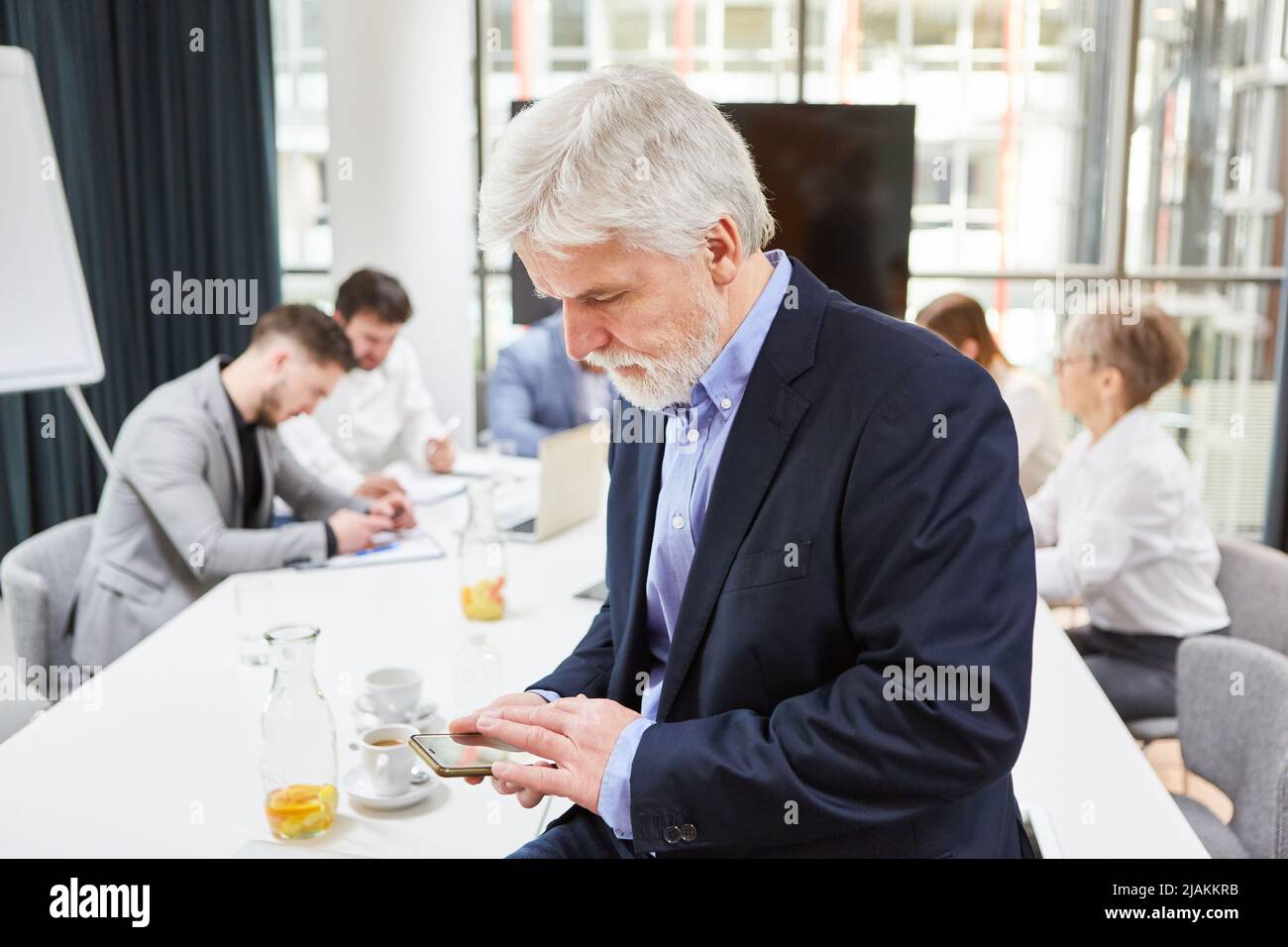 Homme d'affaires lisant des sms ou des informations de flux Web sur un smartphone lors d'une réunion au bureau Banque D'Images