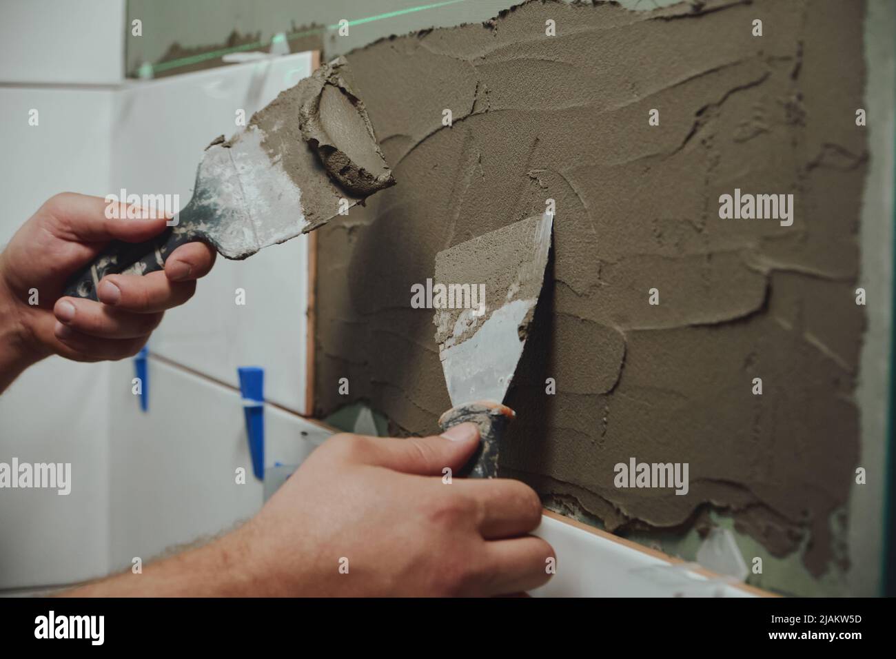 Application de l'adhésif pour carreaux sur le mur de la salle de bains par les mains d'une personne méconnaissable Banque D'Images