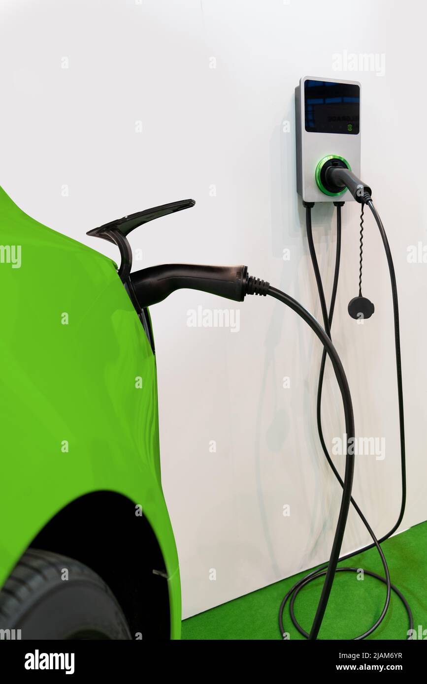 Gros plan d'une voiture électrique verte avec station de charge pour véhicules électriques sur un mur blanc Banque D'Images