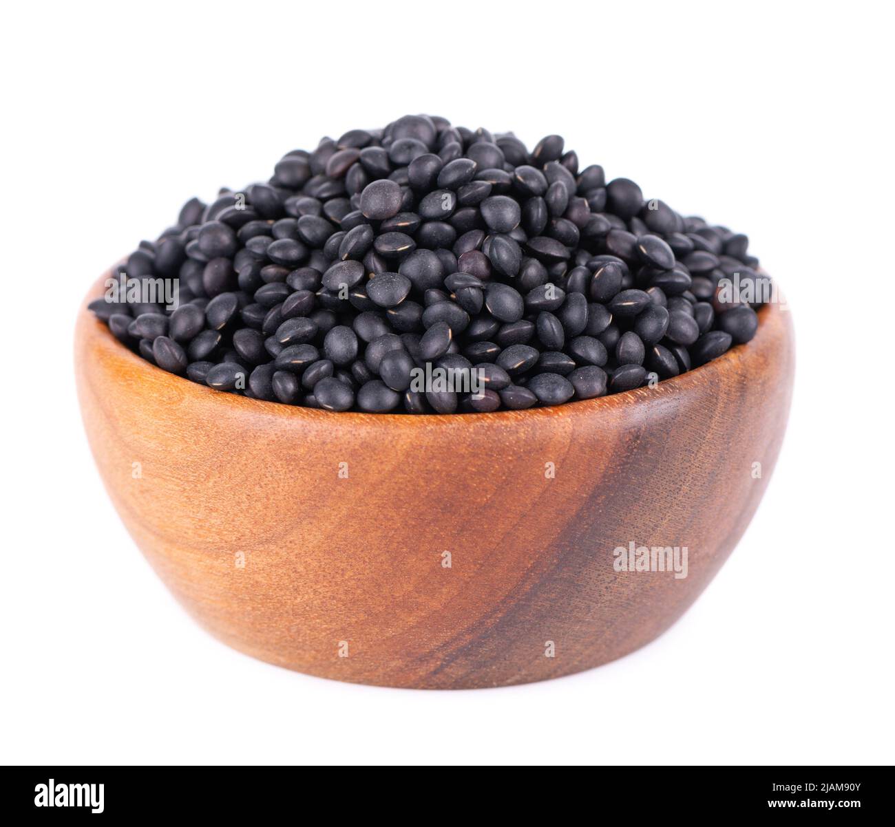 Lentilles noires dans un bol en bois, isolées sur fond blanc. Pile de grains de lentilles de béluga secs Banque D'Images