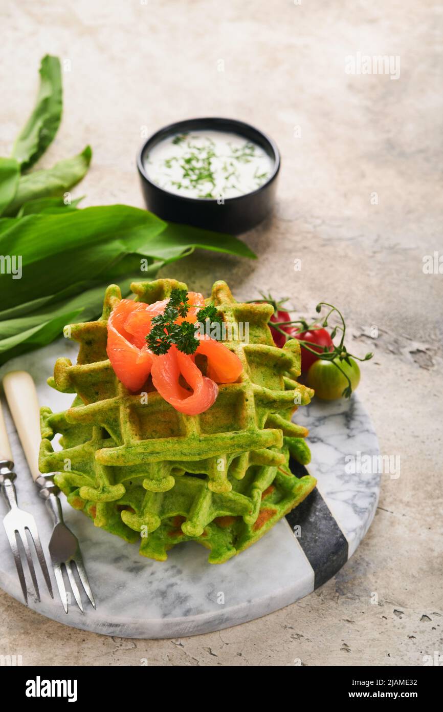 Gaufres belges vertes. Épinards ou ail sauvage ou gaufres au pesto avec saumon rouge et sauce à la crème sur fond de table en béton gris. Délicieux petit déjeuner, Banque D'Images