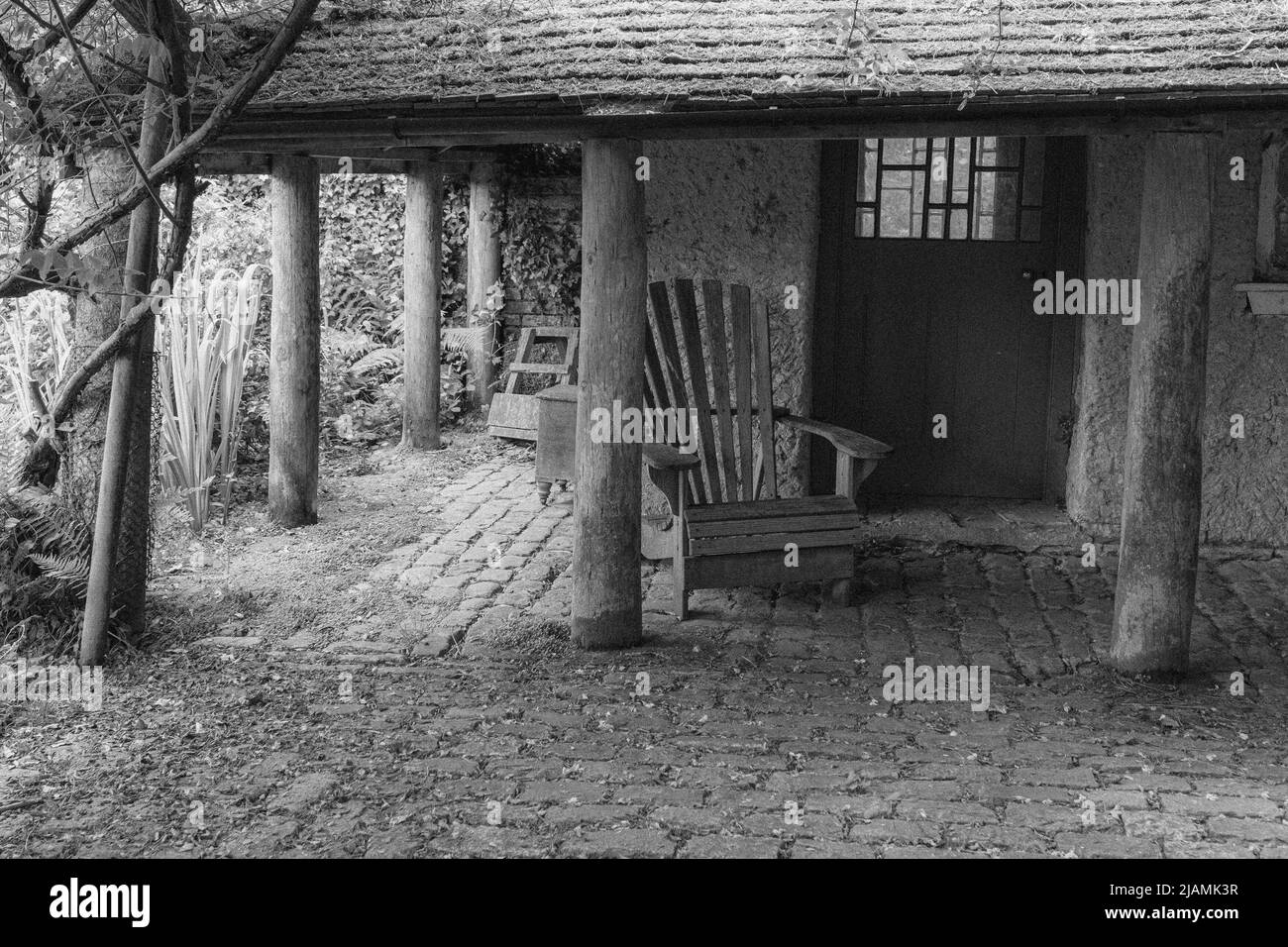 Image intemporelle, nostalgique, de la vieille pierre, hangar en pots aux piliers avec plancher pavé, vieux sièges en bois et wisteria à Trewithen Cornwall Banque D'Images