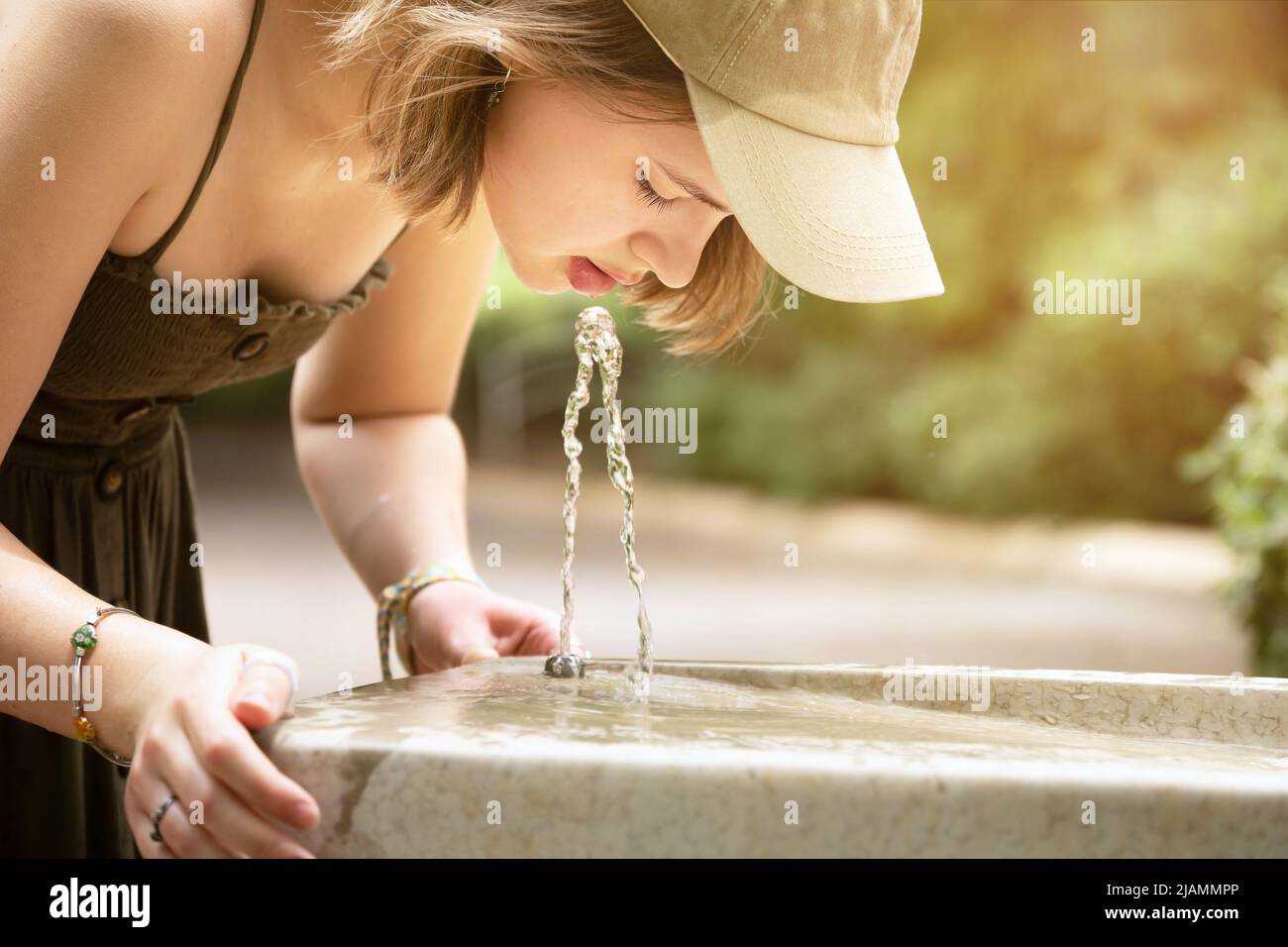 Une adolescente boit de l'eau provenant d'une fontaine extérieure Banque D'Images