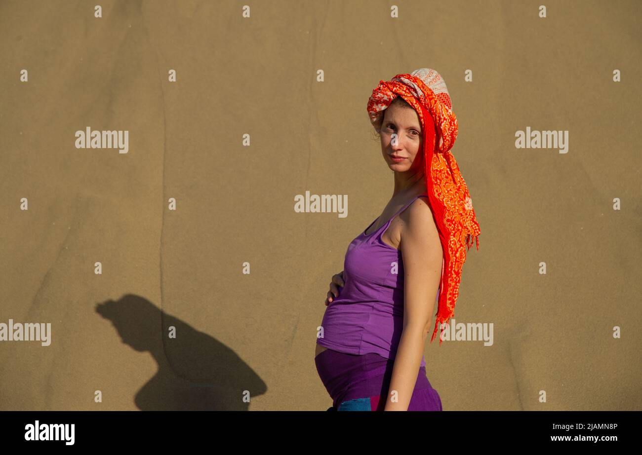 La femme enceinte pose dans les dunes de sable de Maspalomas de Gran Canaria, aux îles Canaries, sur fond de sable doré et de ciel bleu vêtu de lumière vive Banque D'Images