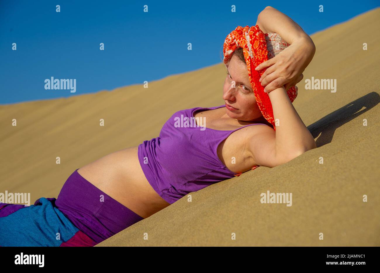 La femme enceinte pose dans les dunes de sable de Maspalomas de Gran Canaria, aux îles Canaries, sur fond de sable doré et de ciel bleu vêtu de lumière vive Banque D'Images