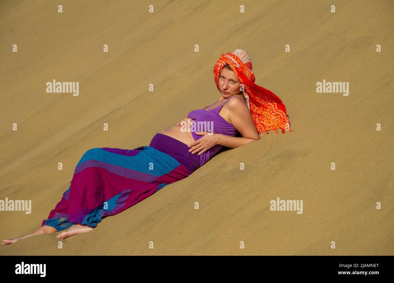 La femme enceinte pose dans les dunes de sable de Maspalomas de Gran Canaria, aux îles Canaries, sur fond de sable doré et de ciel bleu vêtu de lumière vive Banque D'Images