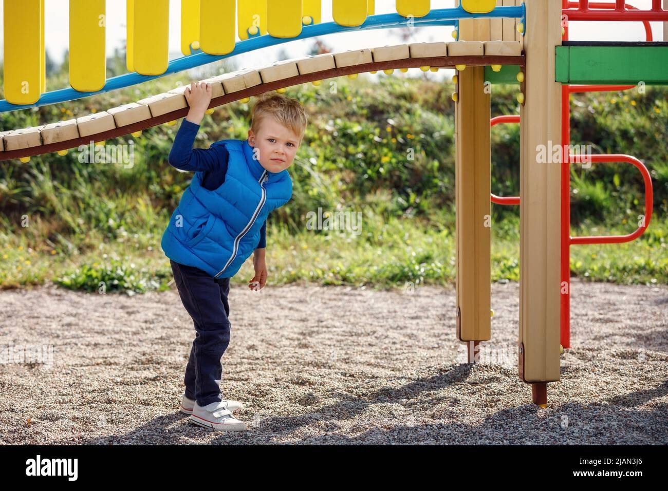 Un petit garçon mignon joue sous un magnifique pont incurvé sur un terrain de jeu coloré. Photo horizontale. Banque D'Images