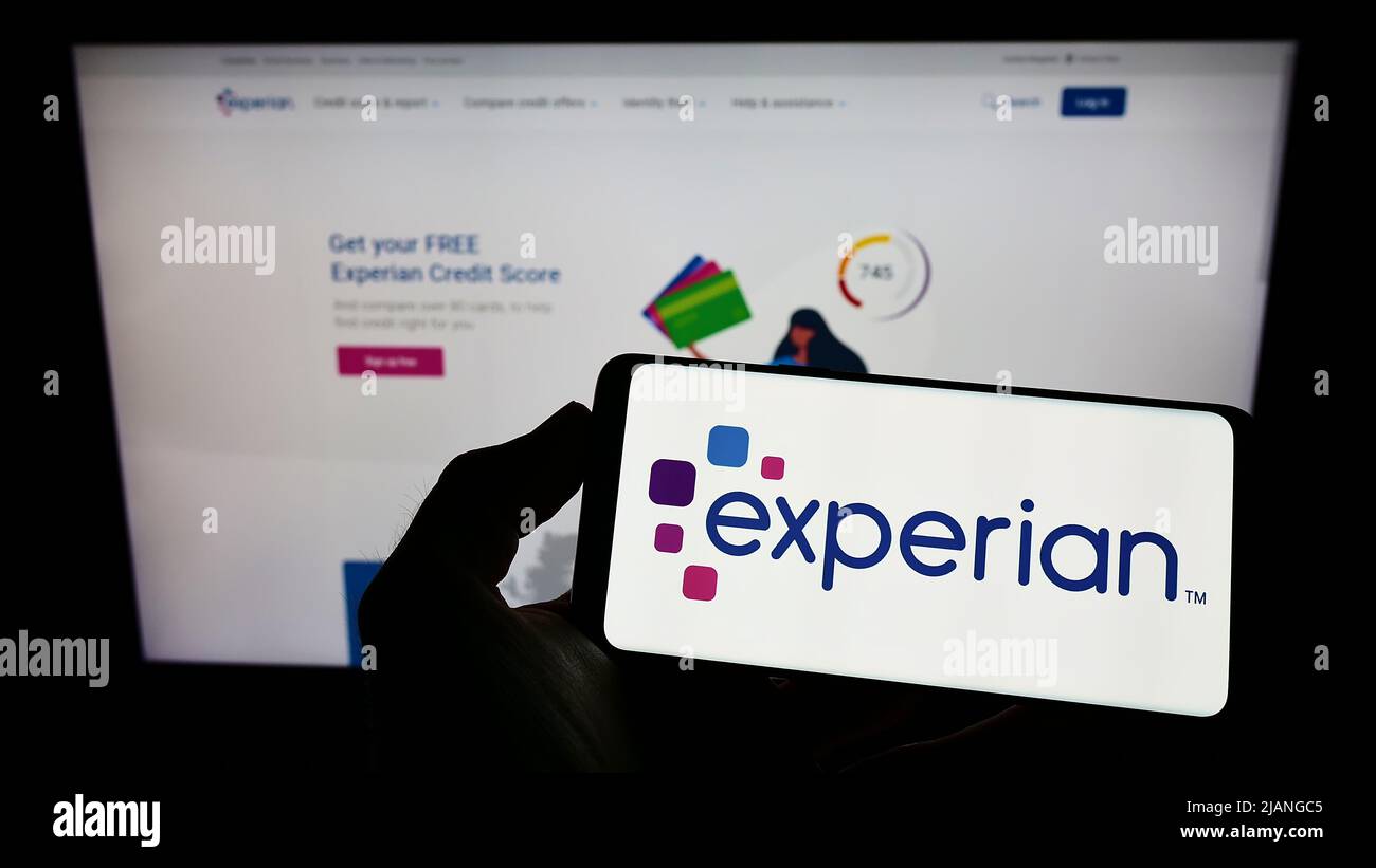Personne détenant un téléphone portable avec le logo de la société d'évaluation de crédit Experian plc à l'écran en face de la page Web de l'entreprise. Mise au point sur l'affichage du téléphone. Banque D'Images