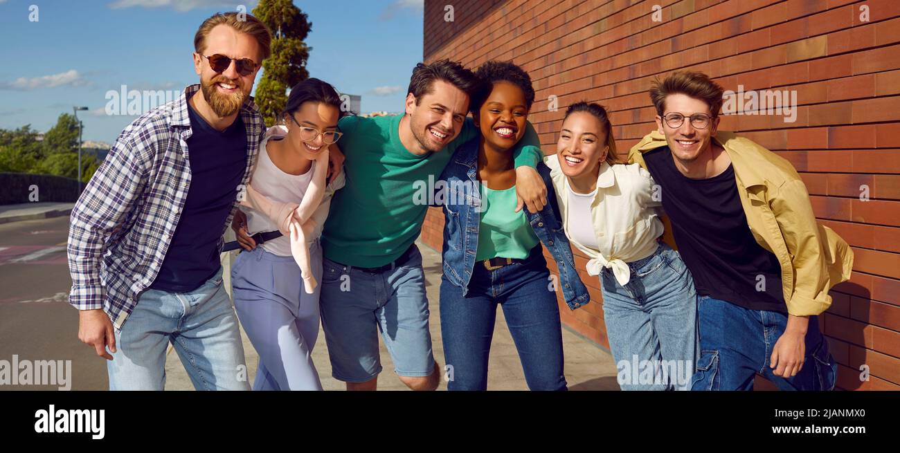 Groupe de jeunes amis multiethniques gaies debout dans la rue, embrassant et souriant Banque D'Images