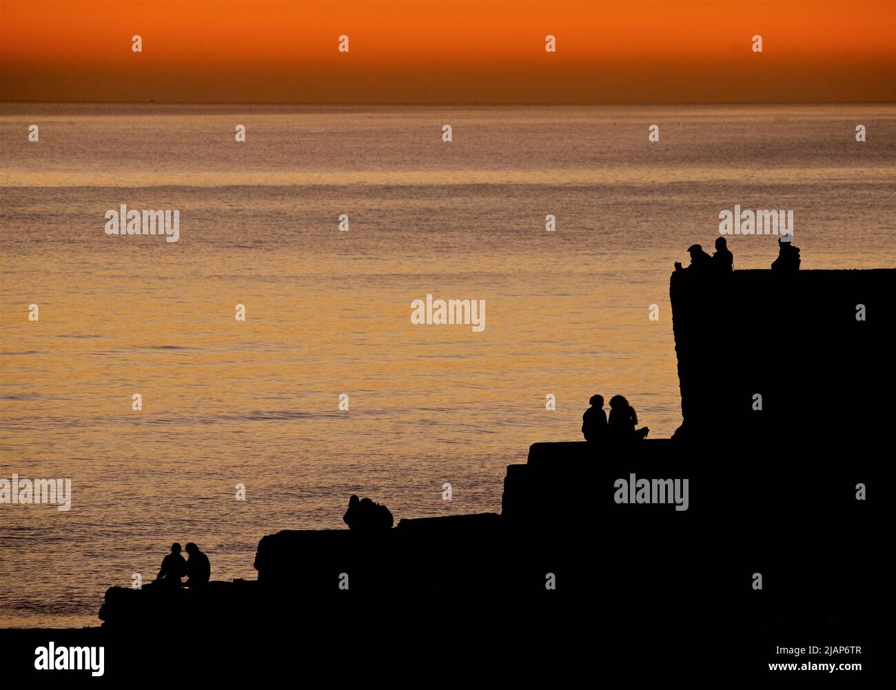 Silhoueted formes de personnes assises et debout sur une groyne sur Brighton Beach, après avoir regardé le coucher du soleil. Le ciel s'éveille avec la lumière du jour. Brighton, Angleterre, Royaume-Uni Banque D'Images
