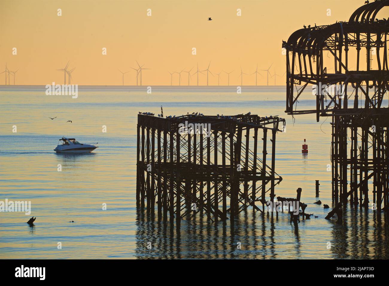 Détail de la structure en fer abandonnée et désintégrée de West Pier au crépuscule, Brighton. Construit en 1866 et fermé en 1975, le quai est toujours classé de catégorie I et un site bien connu. Le parc éolien offshore de Rampion peut être vu à l'horizon. Les oiseaux marins s'assoient sur la jetée. Passage d'un petit bateau à moteur Banque D'Images