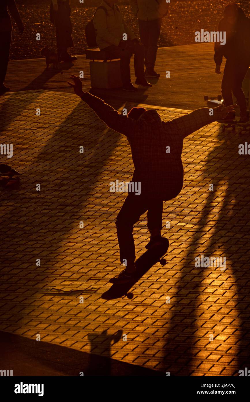 La silhouette d'un jeune homme qui réalise un tour de skateboard au coucher du soleil à côté de West Pier et i360 sur l'esplanade inférieure de Brighton. Brighton & Hove, Royaume-Uni Banque D'Images