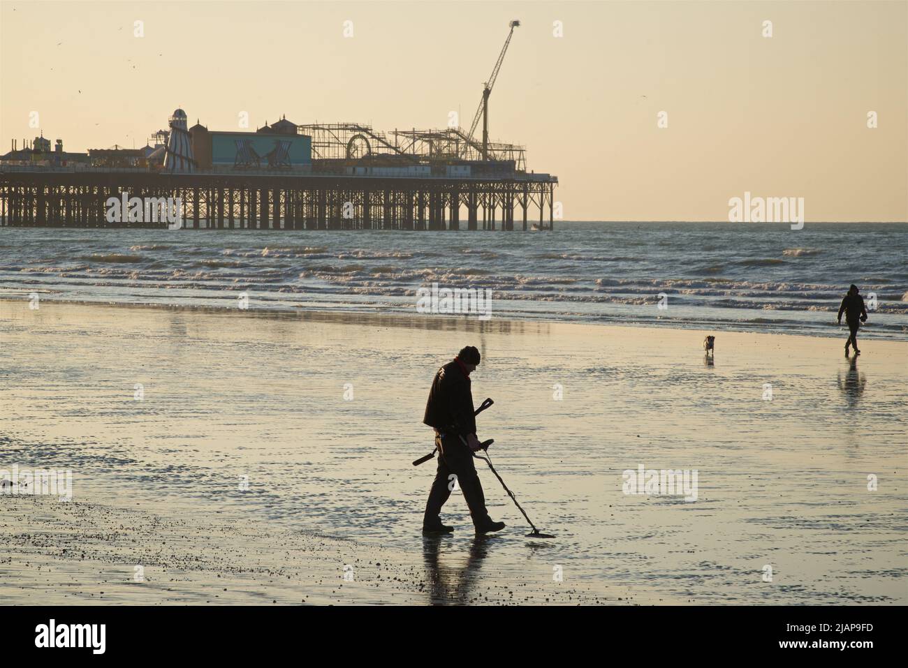 La prospection de détect. Métal sur le sable à faible temps. Beach at Dawn, Brighton & Hove, Sussex, Angleterre, Royaume-Uni. PPeople marchant sur le sable, certains avec un chien; Palace Pier au-delà. Banque D'Images