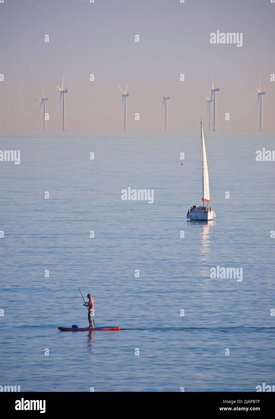 Turbines du parc éolien offshore de Rampion situé au large de la côte de Sussex, Angleterre, Royaume-Uni. Mise en service et production d'énergie renouvelable en 2018, la construction du parc d'éoliennes de 116 a coûté £1,3 000. Yacht au milieu du sol; paddleboarder au premier plan. Banque D'Images