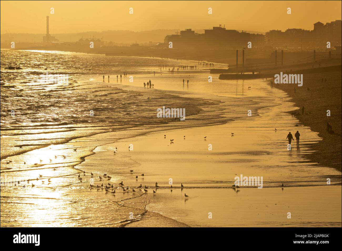 Silhoueted formes de personnes sur la plage à marée basse, Brighton & Hove, East Sussex, Angleterre, Royaume-Uni. Les piliers verticaux au-delà à droite représentent les vestiges de l'ancien West Pier. Shoreham Power Station au loin. Banque D'Images