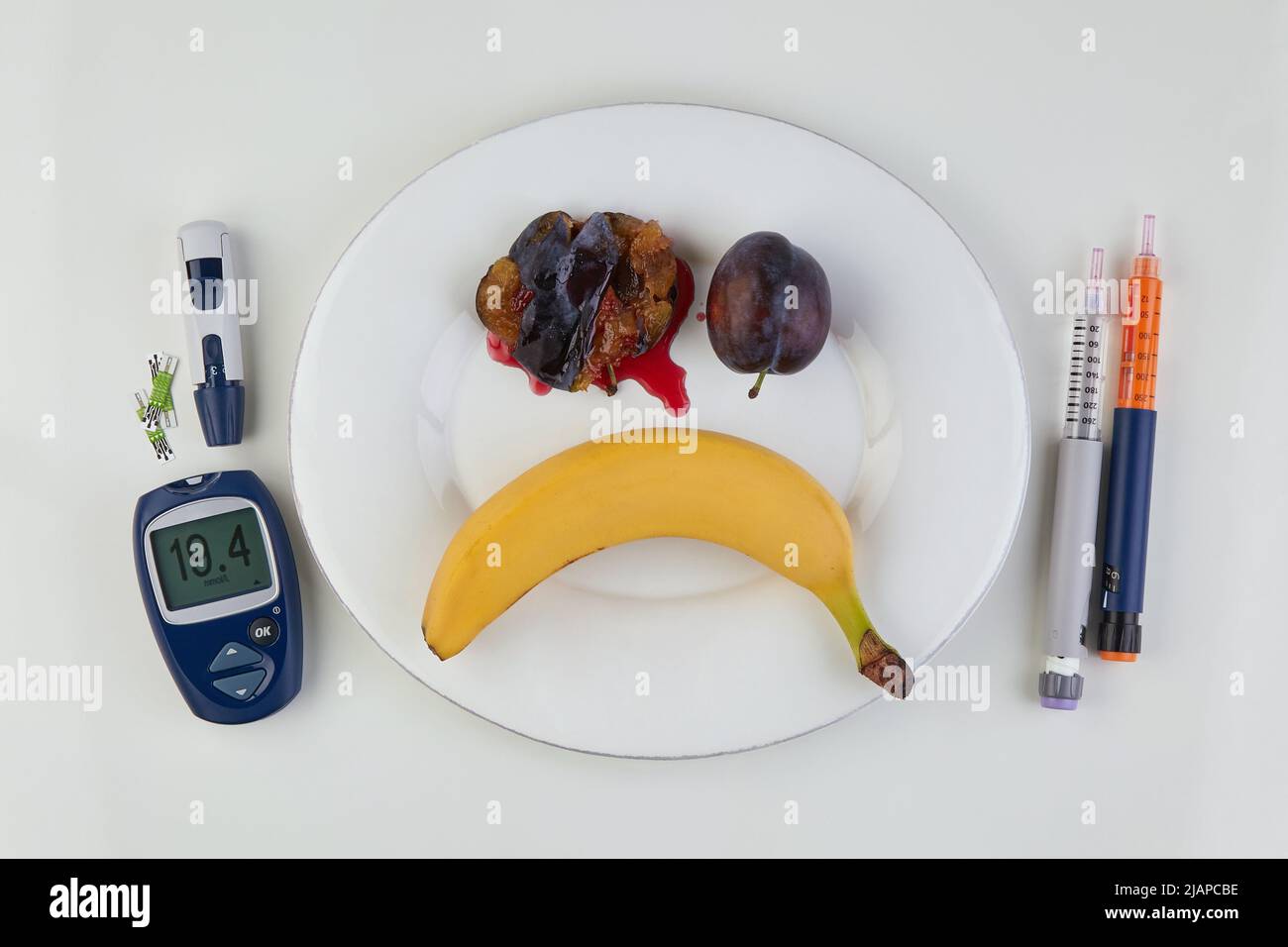 Banane et pêches sous la forme d'une émoticône d'horreur sur une plaque blanche et des stylos à seringue d'insuline et un glucomètre comme coutellerie sur une table en marbre. Di Banque D'Images