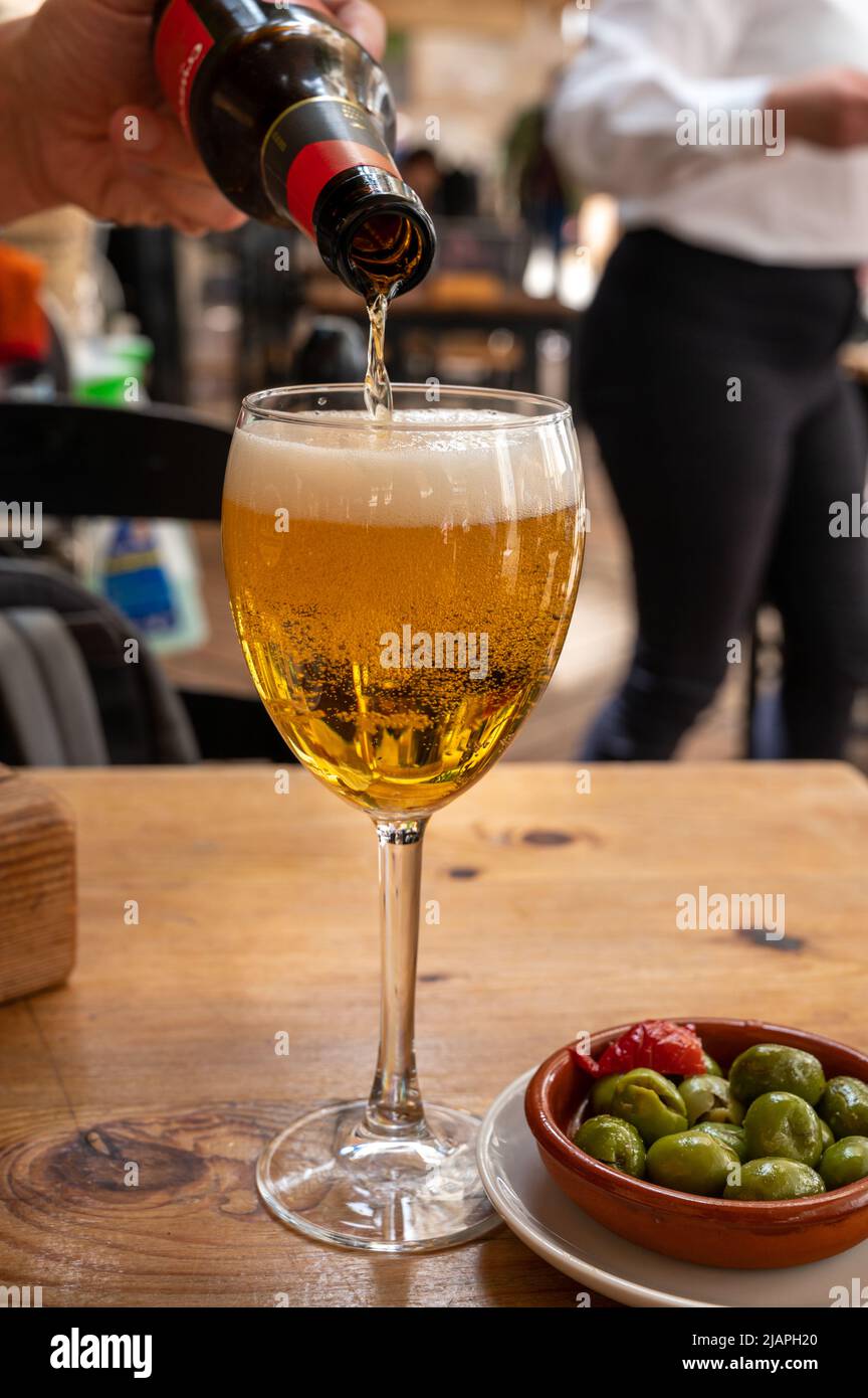 Verser la bière de la bouteille dans le café en plein air espagnol et le bol à tapas avec des