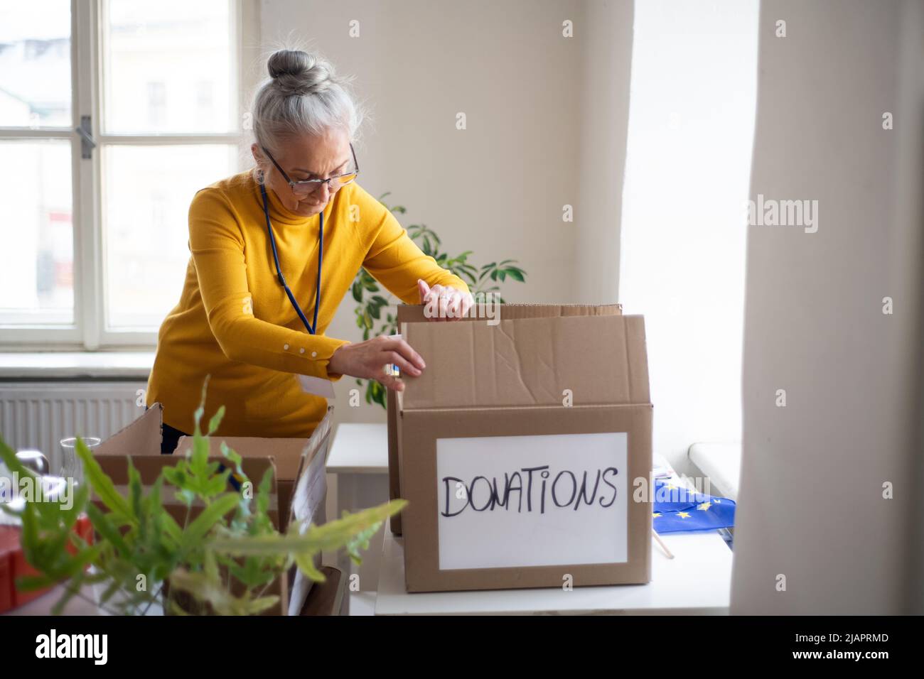 Une femme volontaire senior emballant une boîte avec une aide humanitaire pour les réfugiés ukrainiens en fonction Banque D'Images