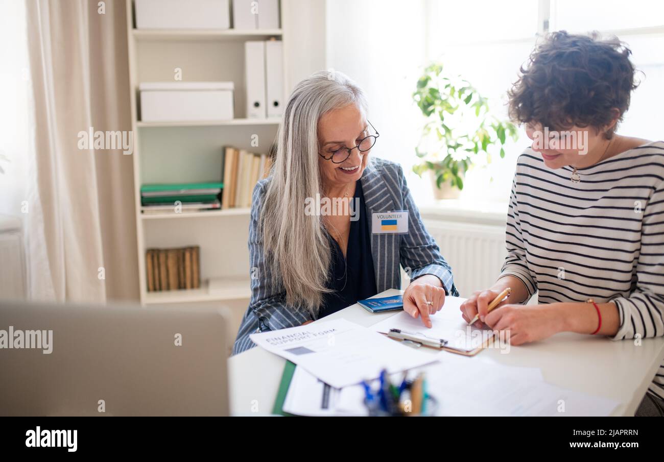 Une femme âgée volontaire aide une femme ukrainienne à remplir des formulaires au centre d'asile. Banque D'Images