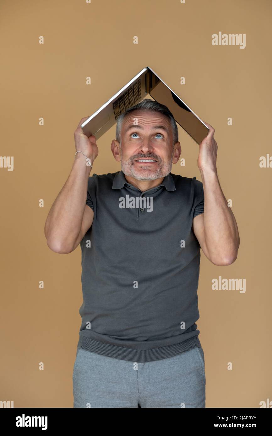 Un homme tenant son ordinateur portable sous la tête et regardant stressé Banque D'Images