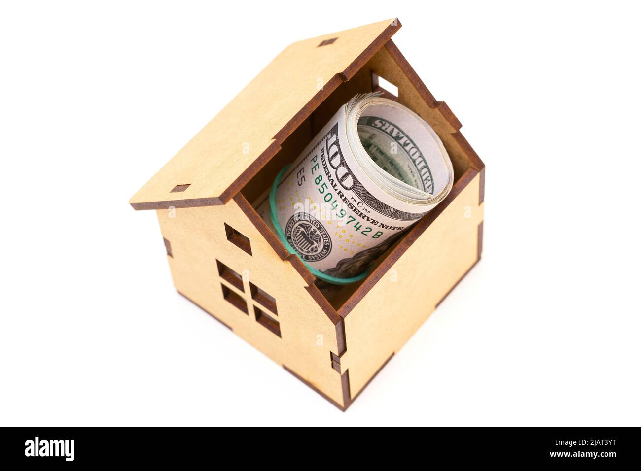 Des billets de cent dollars roulés à l'intérieur d'un modèle de maison en bois isolé sur blanc. Concept d'investissement domestique. Banque D'Images