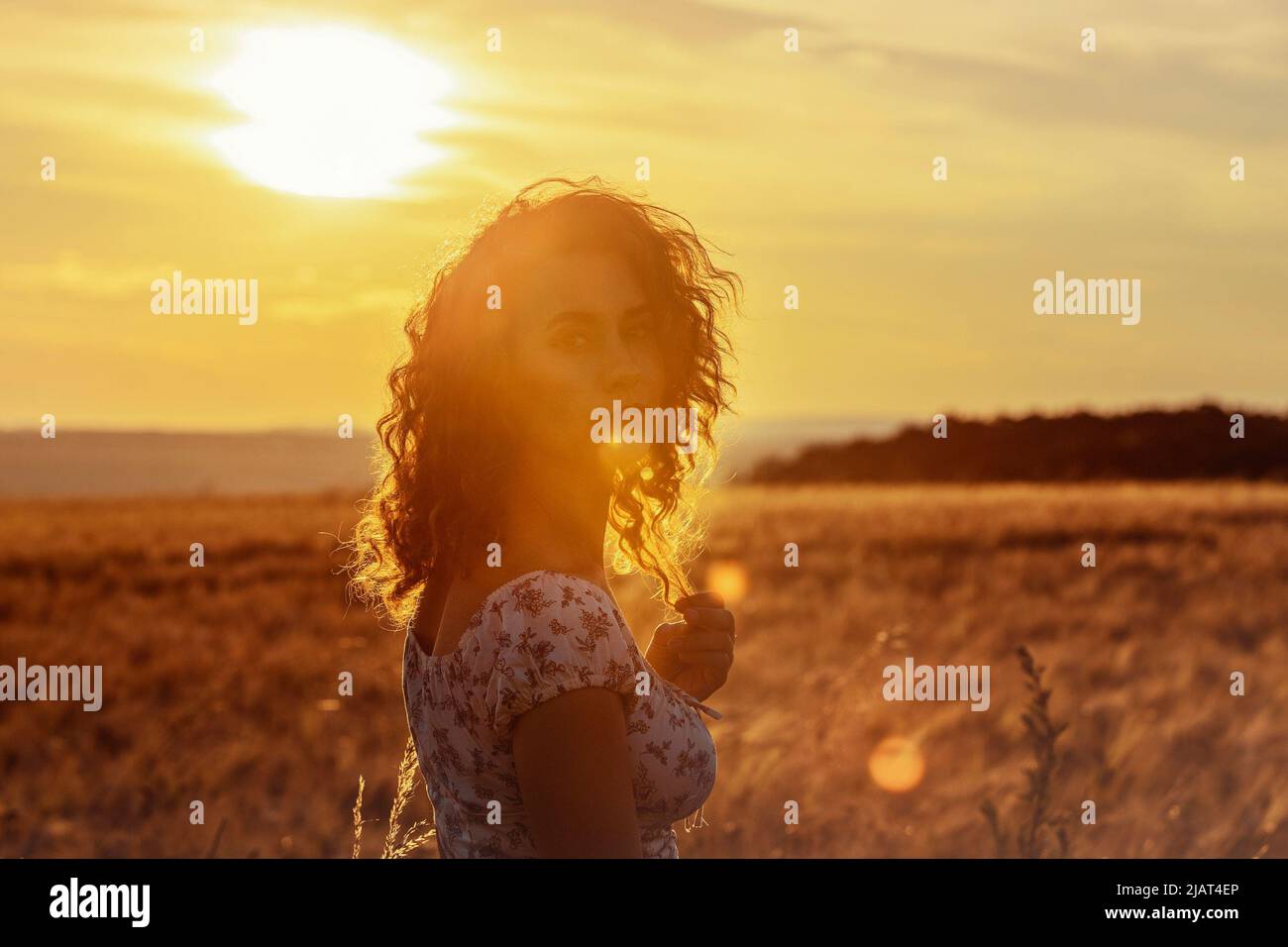 jeune femme marocaine, avec des cheveux bruns, debout dans un champ de blé, tandis que le soleil se pose en arrière-plan et aveuglant la caméra Banque D'Images