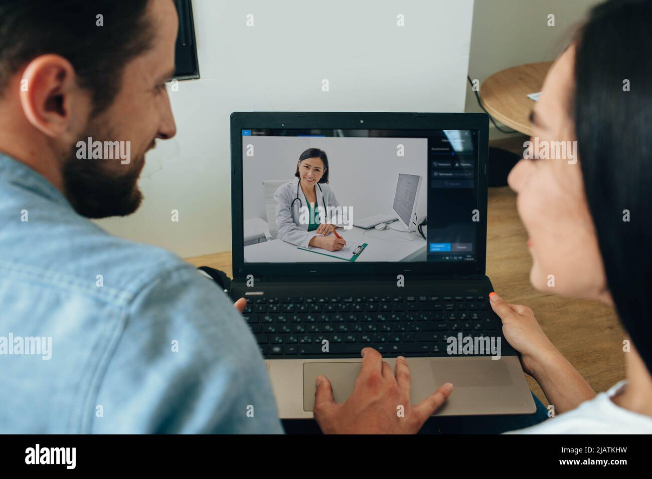 Jeune famille, homme et femme pendant la conférence médicale en ligne et la consultation avec leur médecin de famille. Vidéoconférence avec un médecin Banque D'Images