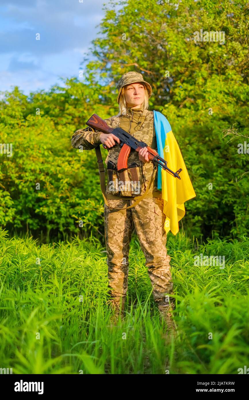 Femme pleine longueur soldat avec arme à feu et drapeau ukrainien sur l'épaule en regardant loin Banque D'Images