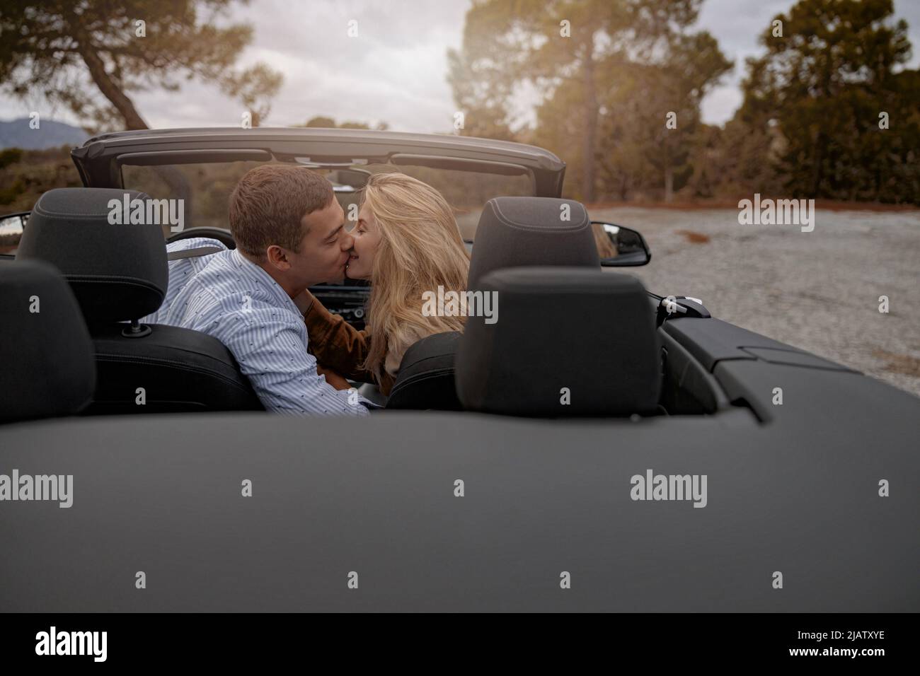 Homme heureux et belle femme assis dans une voiture décapotable en plein air et embrassant, concept d'amour Banque D'Images
