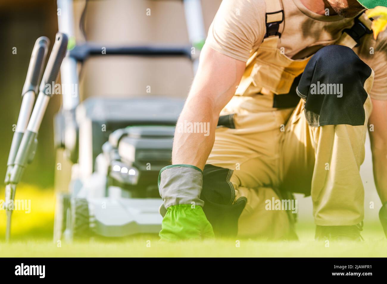 Responsable des paysages caucasiens inspectant l'herbe de jardin pour les maladies, les ravageurs et les patchs secs. Tondeuse à gazon et ciseaux en arrière-plan. Banque D'Images