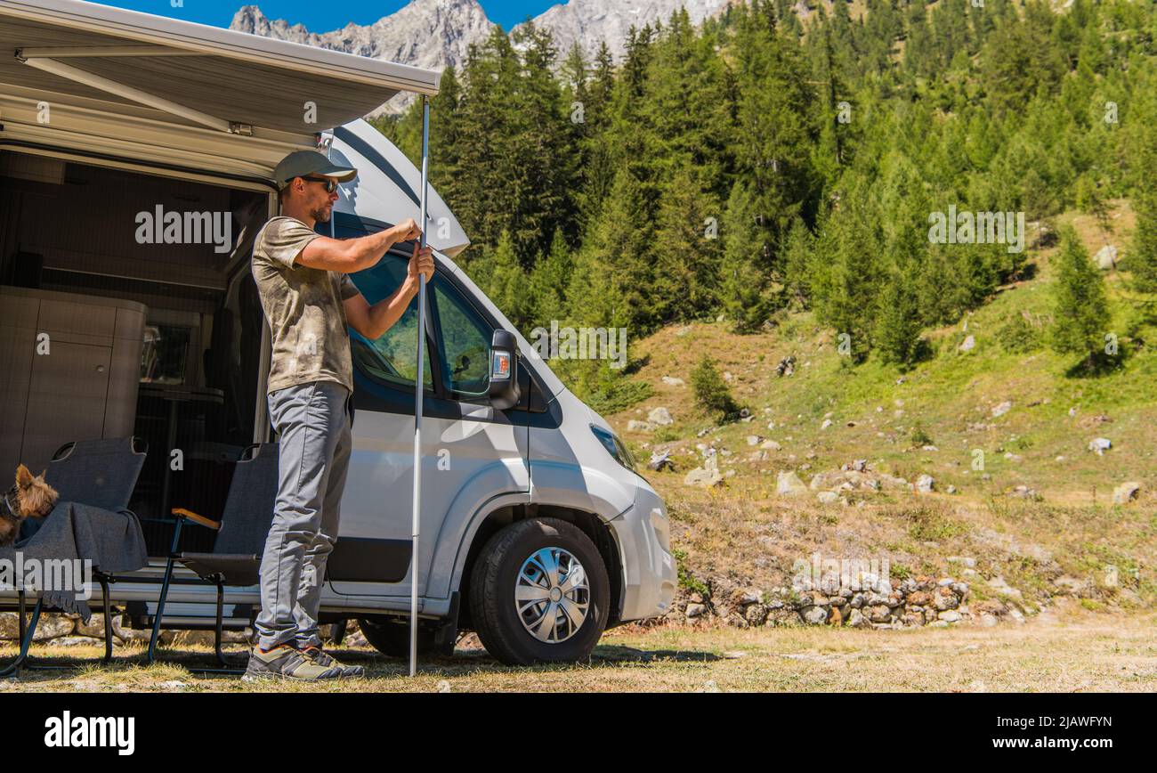 Les hommes déploient et rétracteront l'auvent de la fourgonnette camping-car. Configuration du camping alpin d'été. Véhicules récréatifs thème. Banque D'Images