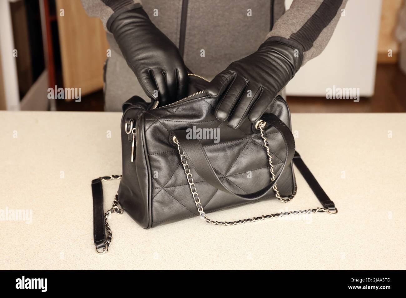 Voleur dans la tenue noire et les gants voir sur ouvert sac de femmes  volées. Un voleur évalue la valeur des objets volés d'un sac à main de  womans dans cuisine interio