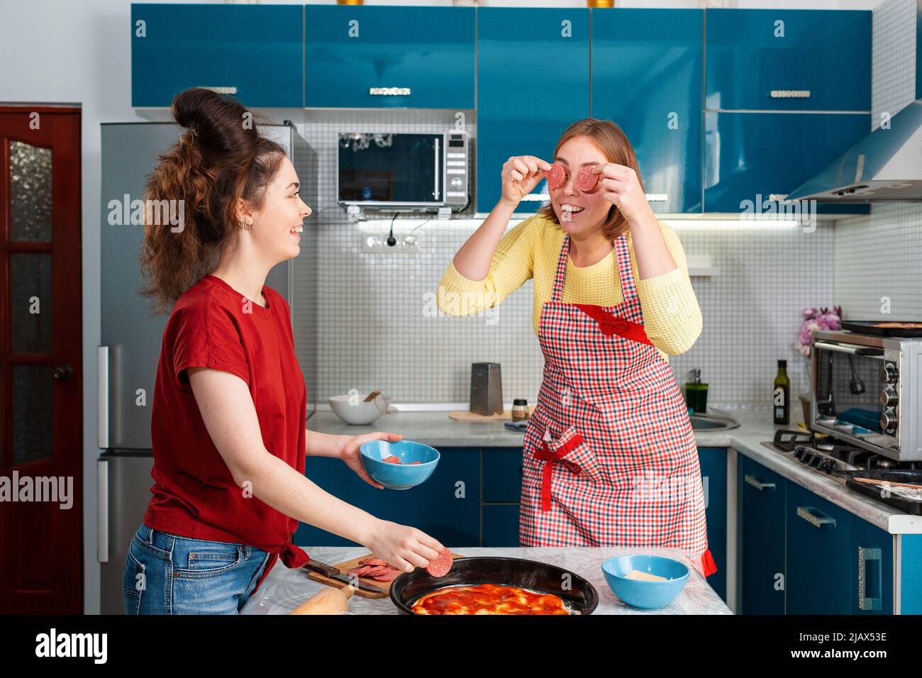 Deux jeunes femmes de race blanche cuisent de la pizza dans la cuisine et s'amusent ensemble. Intérieur. Concept de cuisine à domicile commune pour les couples LGBT. Banque D'Images