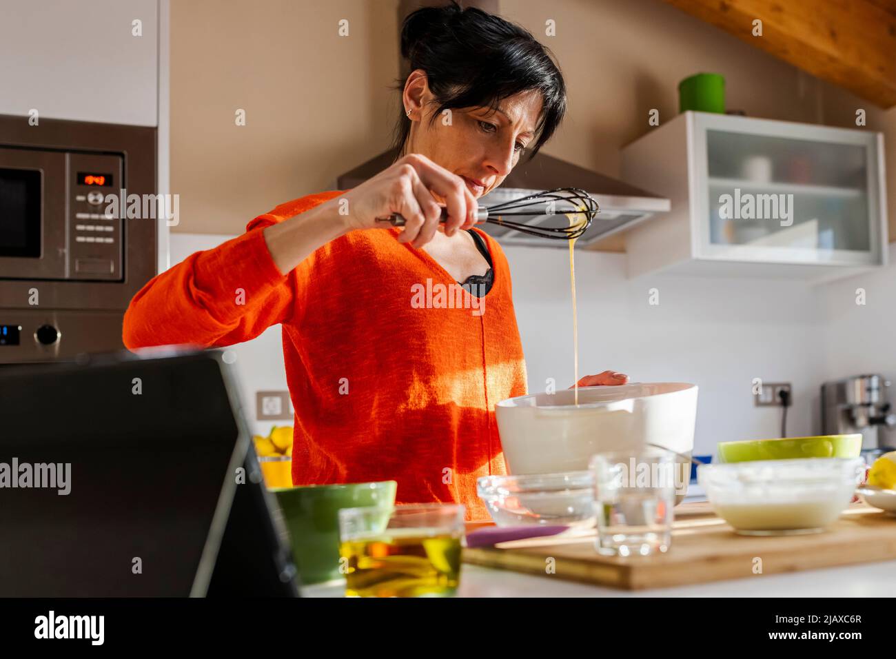 Femme en chandail orange chuchotant des œufs sur un bol blanc. Banque D'Images
