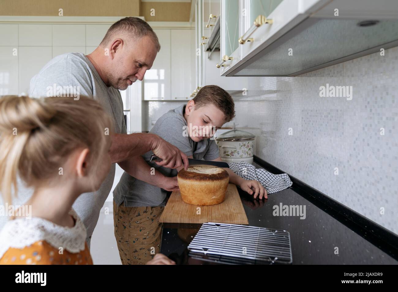 un père avec des enfants coupe du pain frais fait maison. Banque D'Images