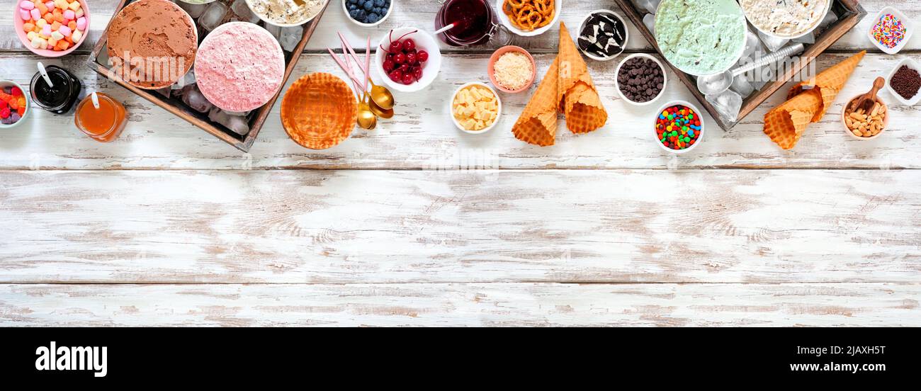 Buffet de glaces d'été avec une sélection de saveurs de glaces et de garnitures de desserts. Vue en hauteur sur la bordure supérieure sur un arrière-plan rustique de bannière en bois blanc. Banque D'Images