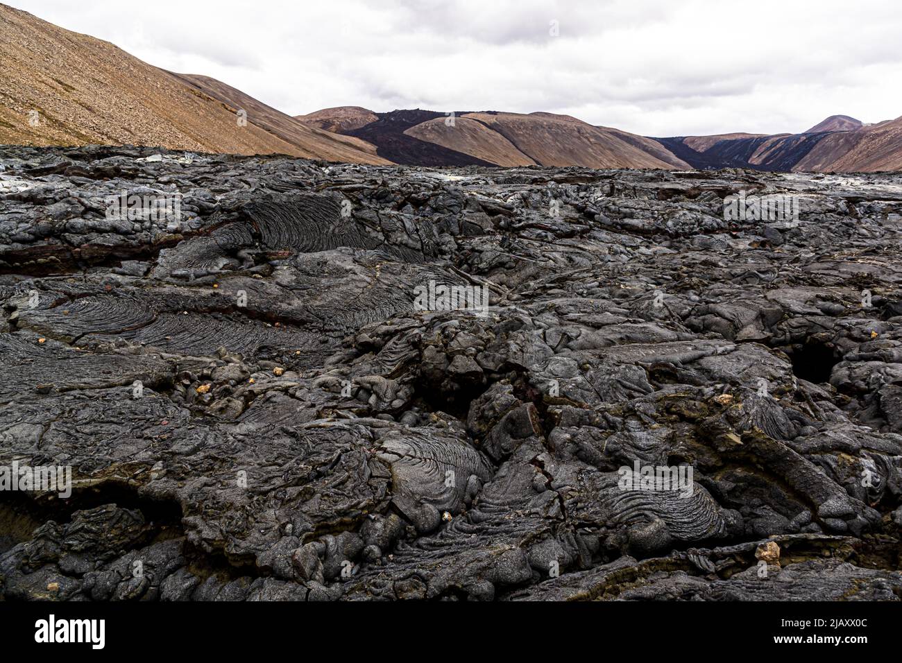 Le roche volcanique grossière et torsadée en forme de corde du volcan Geldingadalir est empilée densément au premier plan ; les pentes brunes du bassin de la vallée de la péninsule de Reykjanes près de Grindavík, en Islande, s'élèvent derrière elle. Le volcan a été actif de mars à septembre 2021 et était alors le plus jeune d'Islande. Banque D'Images