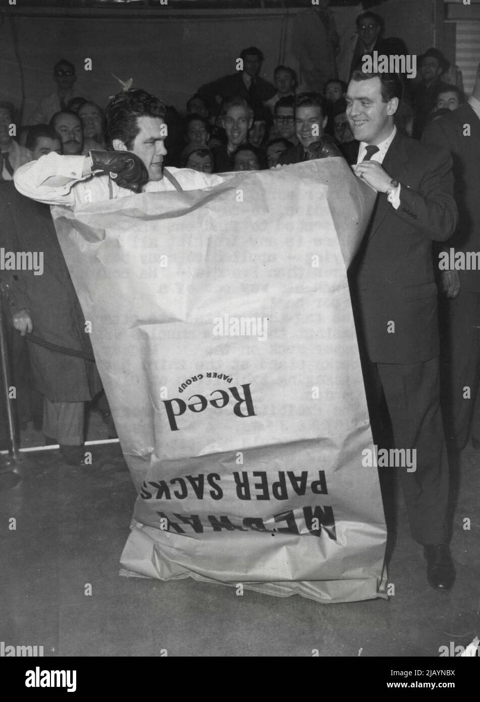 Freddie Mills essaie de se retirer d'un sac en papier -- Un harcelé Freddie Mills pumels sa prison en papier pendant le test de la journée. À droite, le présentateur Eamonn Andrews, qui est lui-même un poids lourd amateur, est le commentateur de la radio. Le sac de punch le plus difficile que j'ai jamais rencontré a été le commentaire de Freddie Mills, l'ancien champion du monde poids lourd léger de Grande-Bretagne, A ce jour (lundi), lorsqu'il a consenti à savoir s'il y a une vérité dans le dicton - appliqué à de nombreux boxeurs autres que Freddie - "il ne pouvait pas se sortir d'un sac en papier". 19 janvier 1953. Banque D'Images