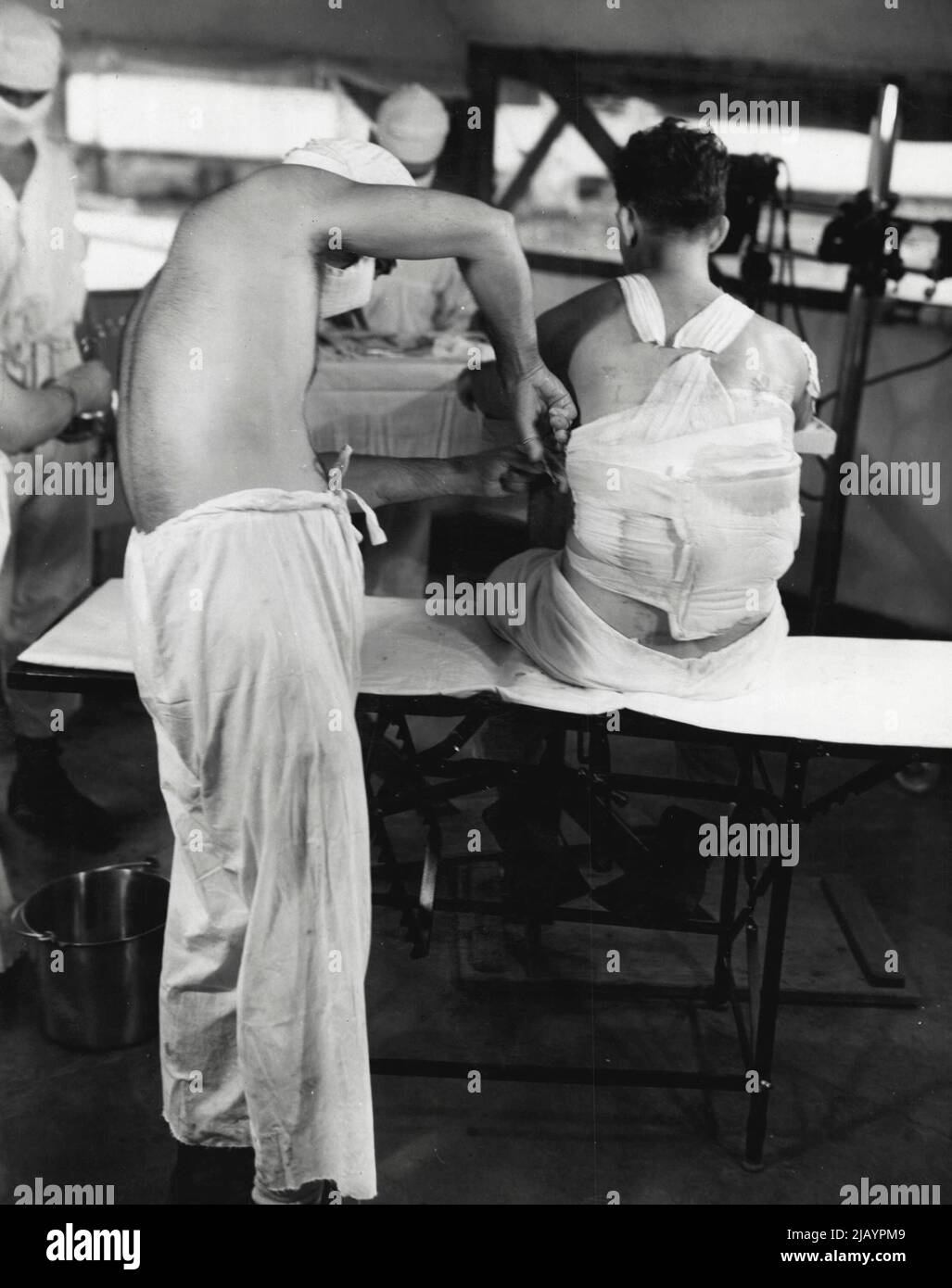 Le médecin d'un hôpital maritime des Solomons se prépare à retirer le bandage d'un patient ayant une blessure d'obus dans son dos afin de lui habiller la plaie. 12 janvier 1944. (Photo de la U.S. Navy Photograph). Banque D'Images