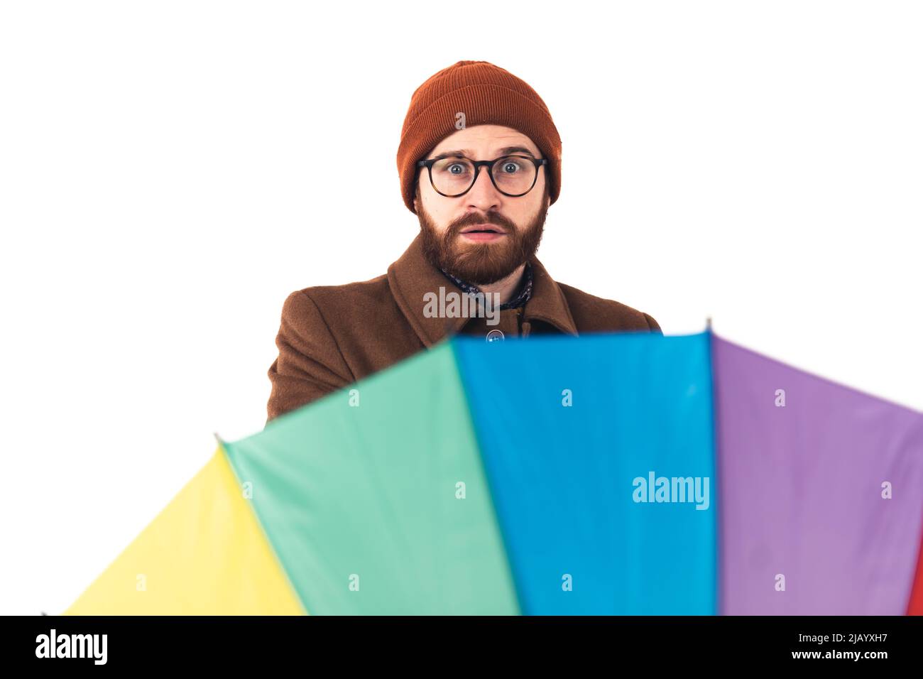 Oh, il pleut à nouveau. Homme barbu européen dans un bonnet choqué derrière un parapluie arc-en-ciel. Concept météo. Studio isolé sur fond blanc. Photo de haute qualité Banque D'Images