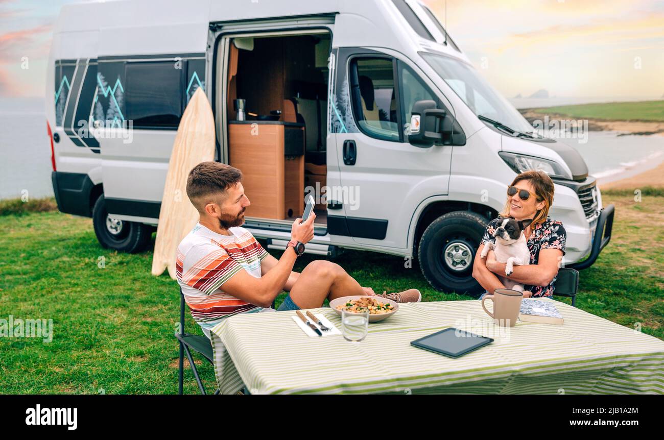 Homme prenant la photo à une femme qui embrasse un chien avec une camionnette et la plage en arrière-plan Banque D'Images