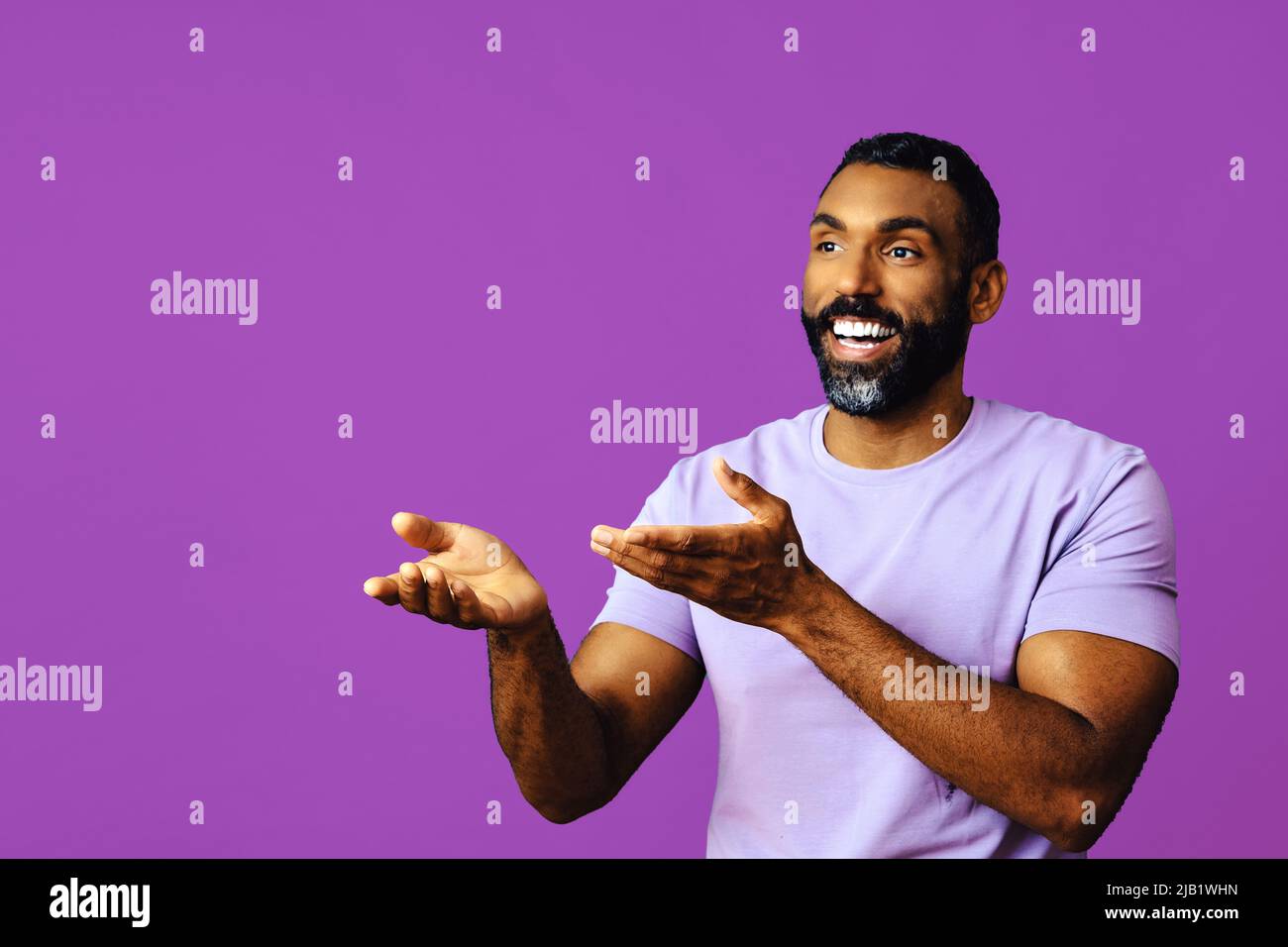 jeune homme noir avec barbe et moustache souriant et regardant loin de l'espace de copie signal main isolé violet arrière-plan studio Banque D'Images